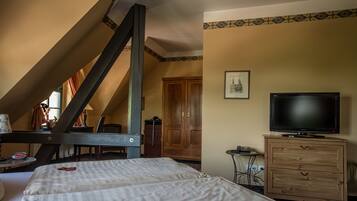 Ein Schlafzimmer mit schrägen Wänden, einem Holzschrank, einem Fernseher und einem Bett mit karierter Bettdecke.
