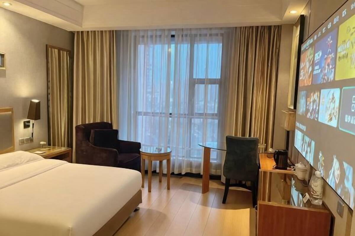Ein Hotelzimmer mit einem Bett, einem Schreibtisch, einem Sessel und einem Fernseher, der verschiedene Bilder zeigt.