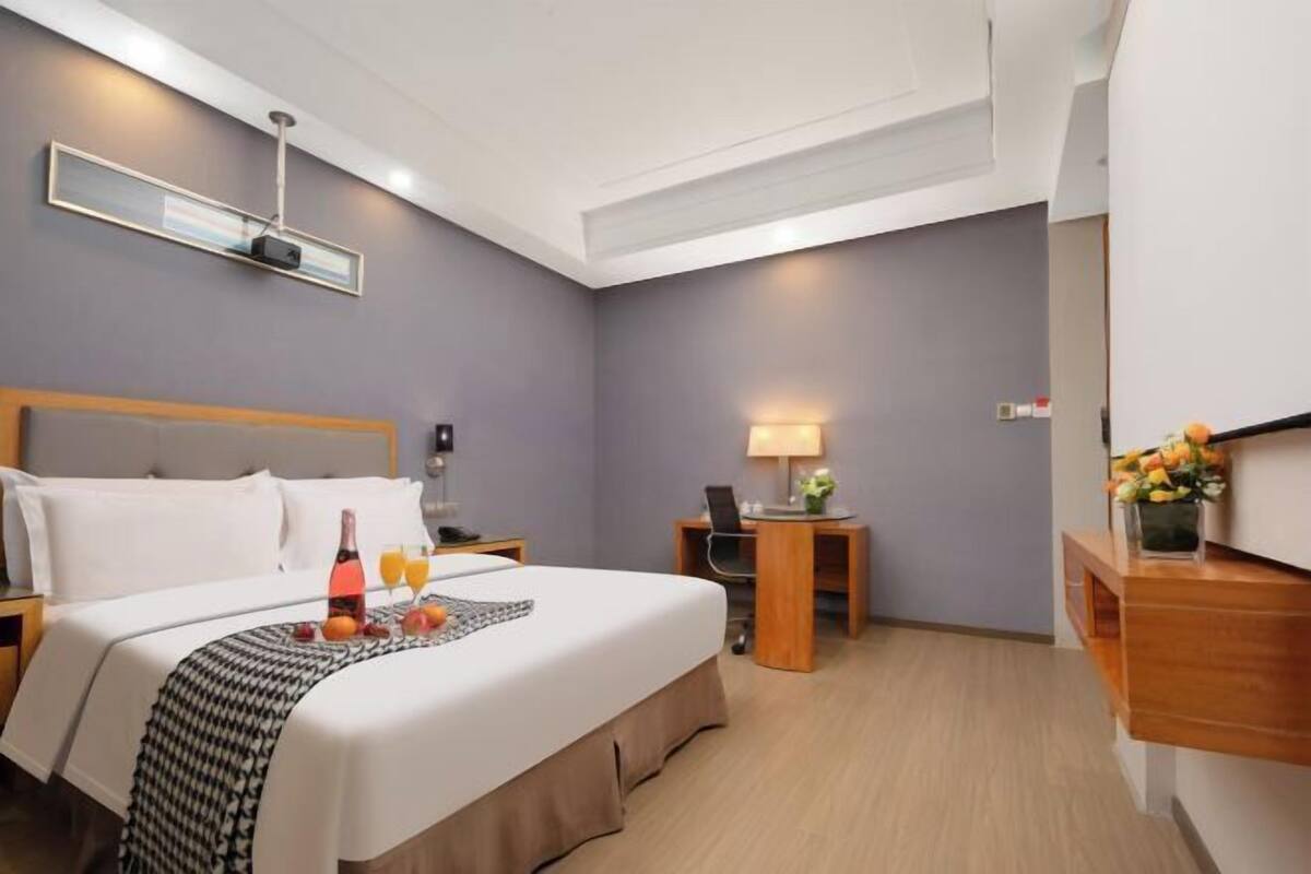 Ein Hotelzimmer mit Bett, Nachttisch, Lampe, Schreibtisch und einer kleinen Pflanze.