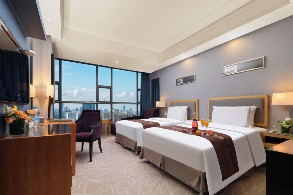 Ein Hotelzimmer mit zwei Betten, einem Schreibtisch, einem Stuhl und Blick auf die Stadt.