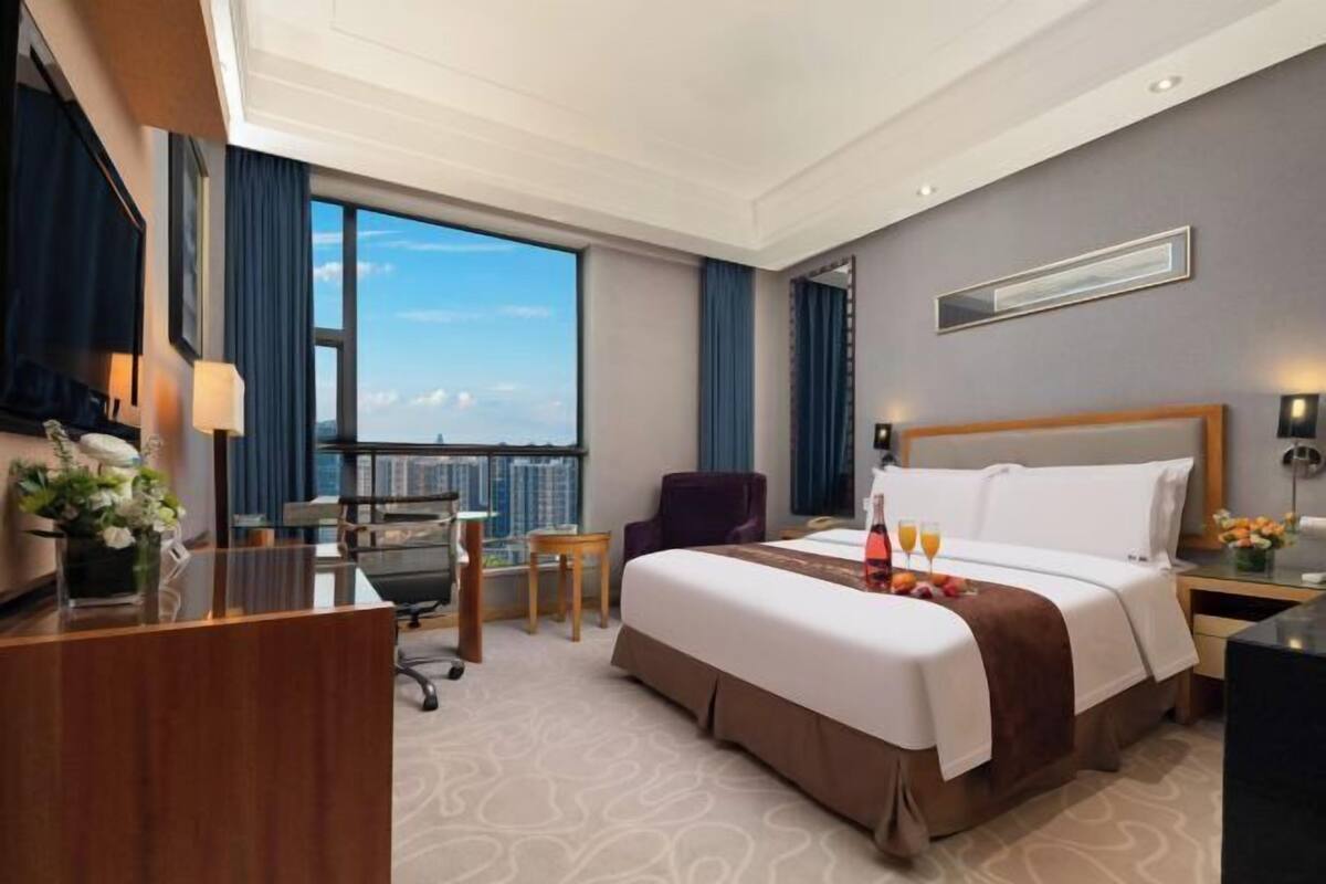 Ein Hotelzimmer mit einem großen Bett, einem Schreibtisch, einem Sessel, einem kleinen Tisch und Blick auf die Stadt.