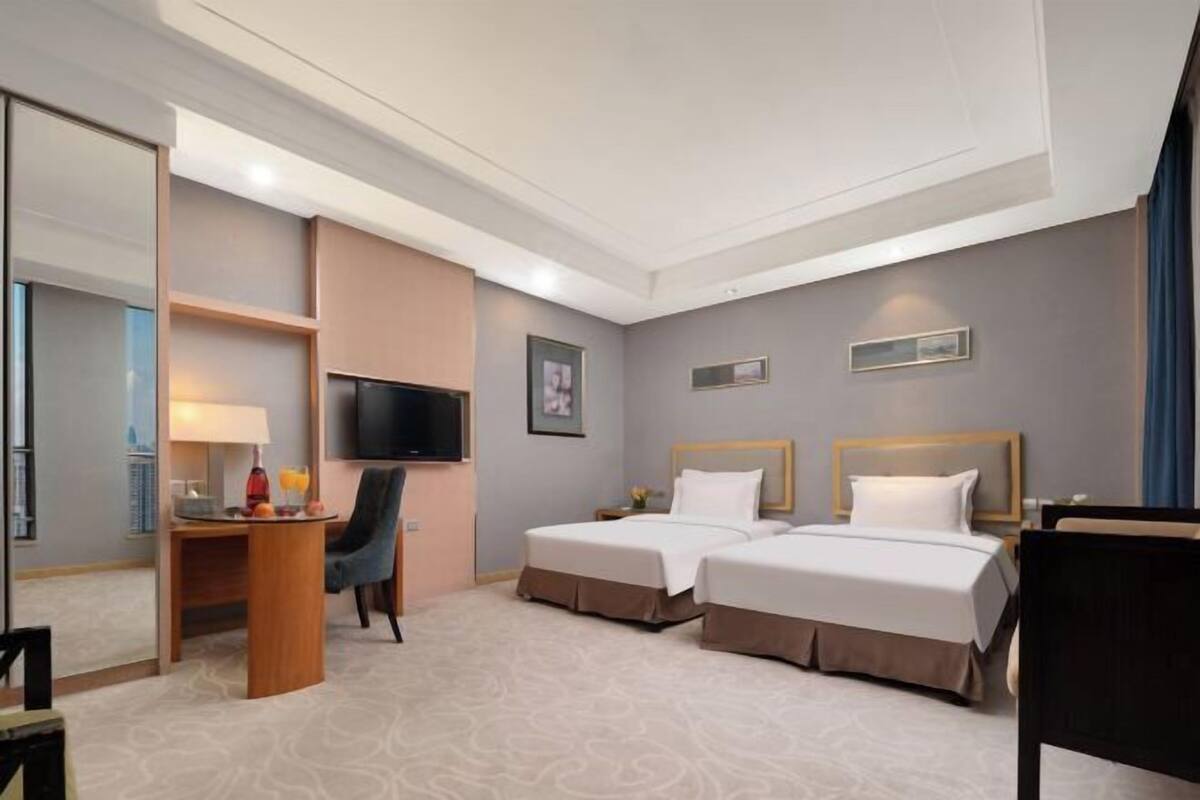Ein Hotelzimmer mit zwei Betten, einem Schreibtisch mit Stuhl, einem Fernseher und einem Spiegel.