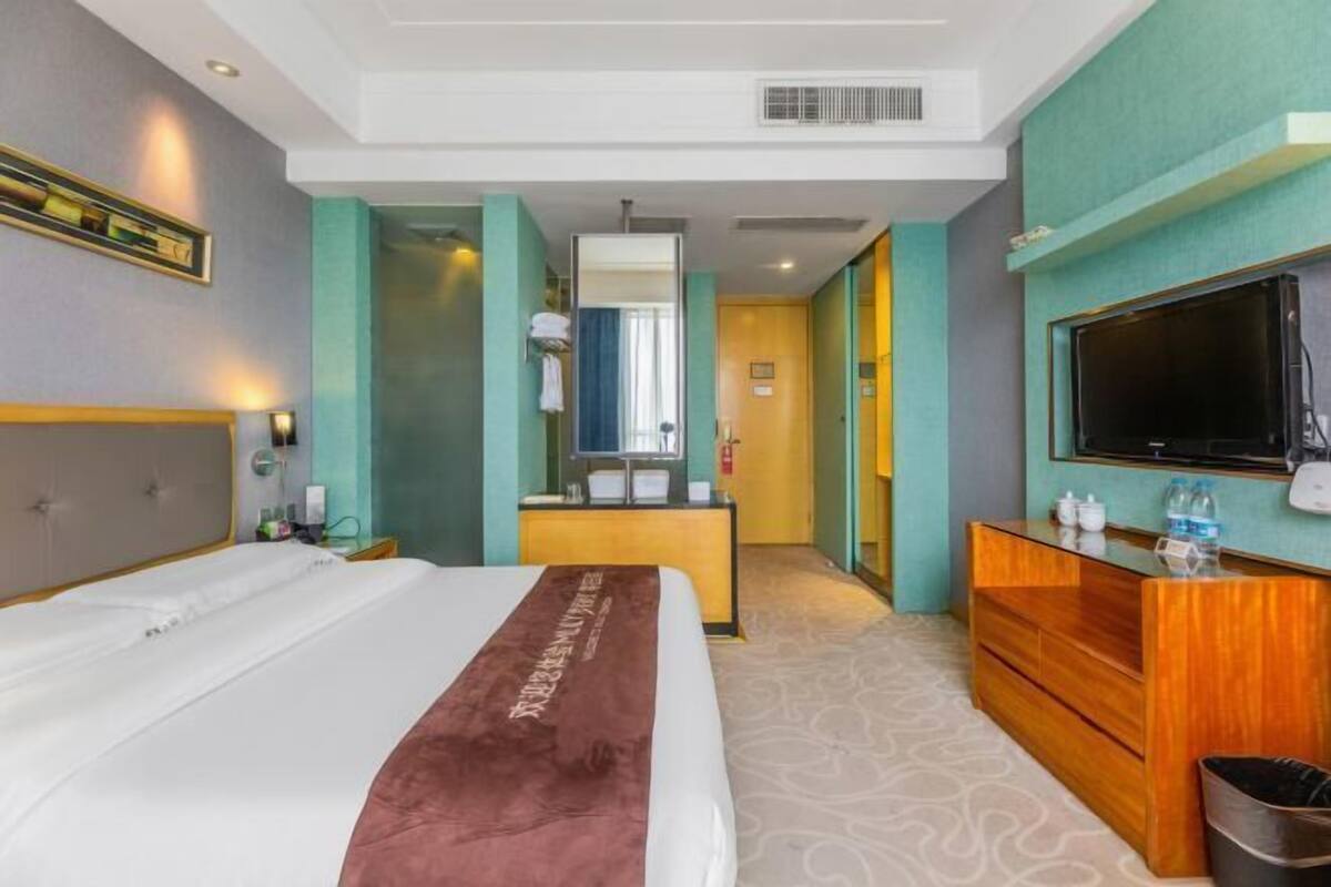 Ein Hotelzimmer mit einem großen Bett, einem hölzernen Schminktisch, einem Fernseher und einem Spiegel.