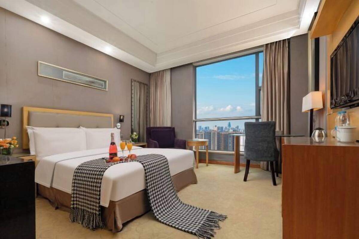 Ein Hotelzimmer mit einem großen Bett, einem Schreibtisch, einem Stuhl, einem kleinen Tisch und Blick auf die Stadt.
