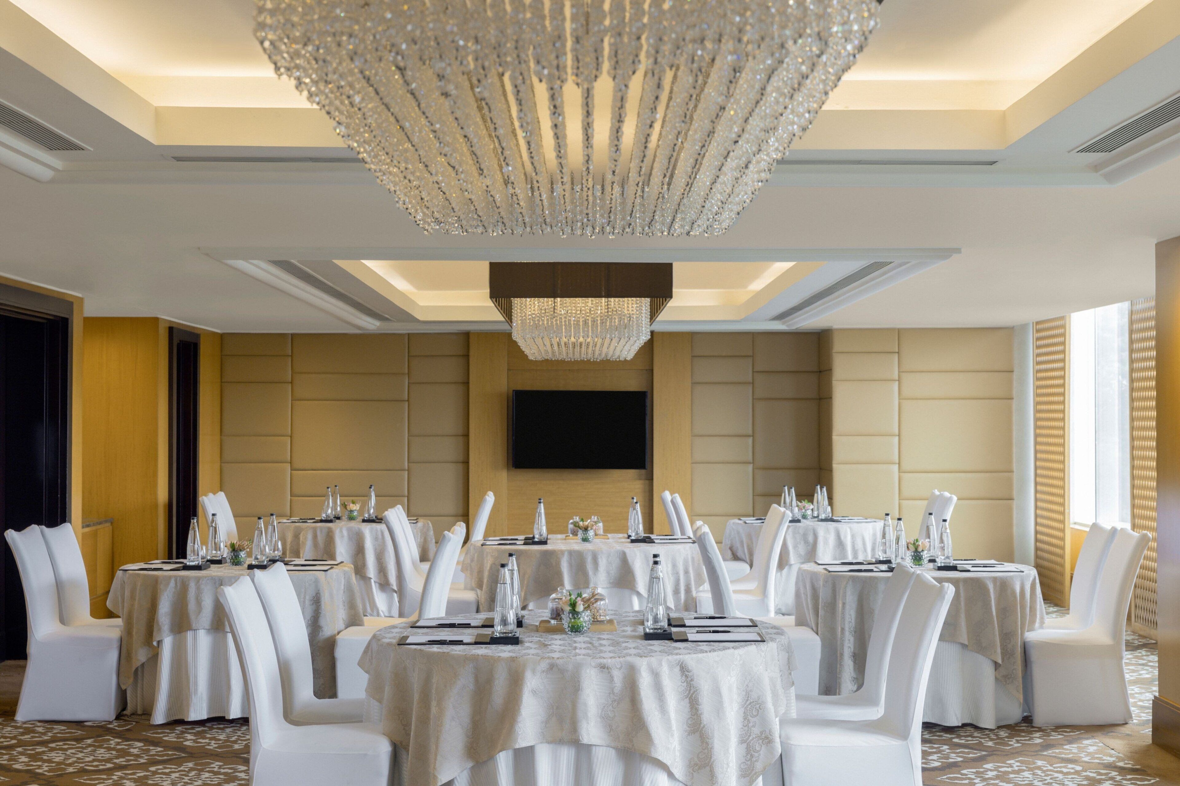 Un salón de banquetes con mesas redondas, sillas blancas y una gran lámpara de araña.