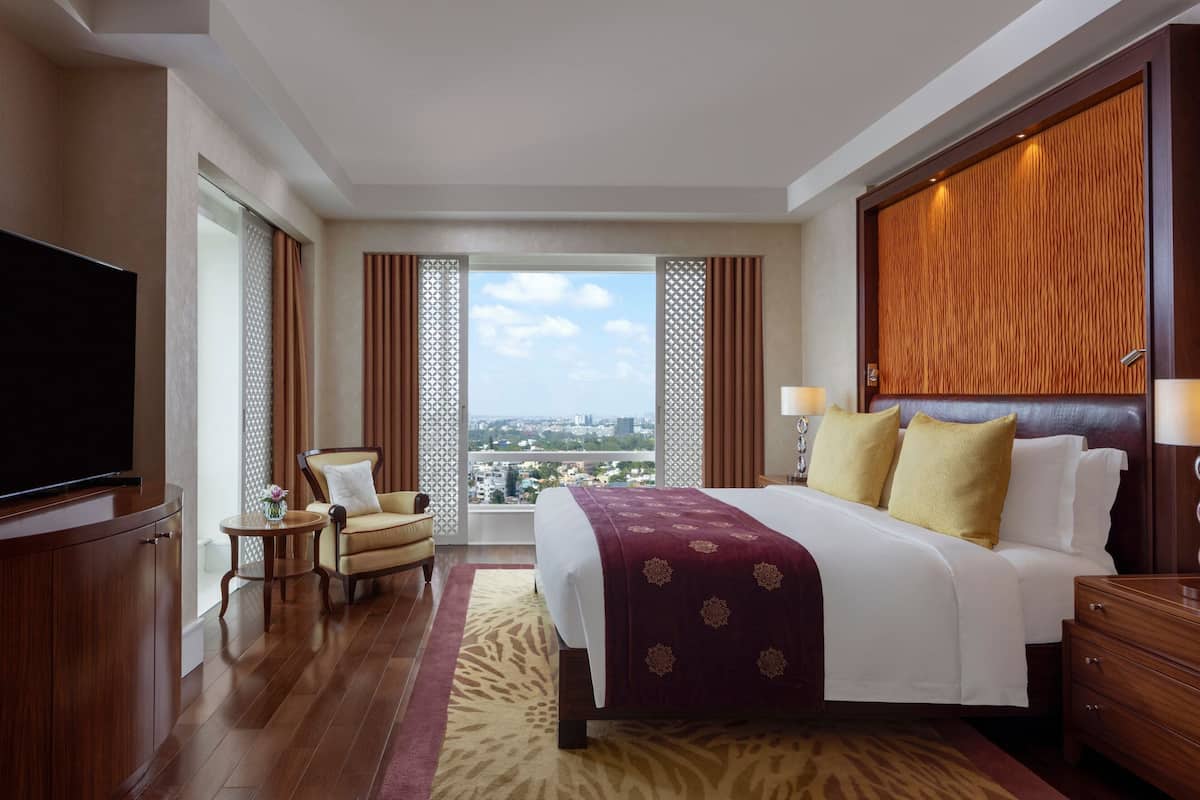 Quarto de hotel com uma cama grande, televisão, área de estar com uma cadeira e vista para a cidade.