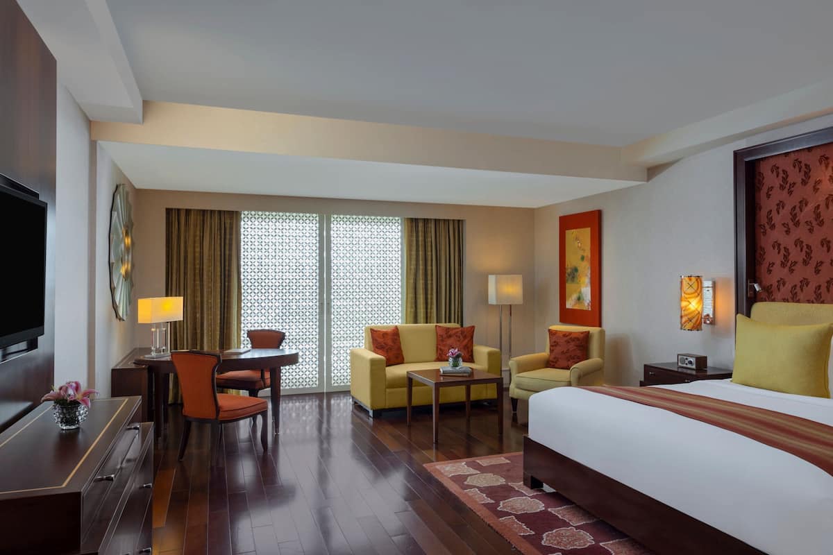 Quarto de hotel com cama, dois sofás, escrivaninha, televisão e janela com cortinas.