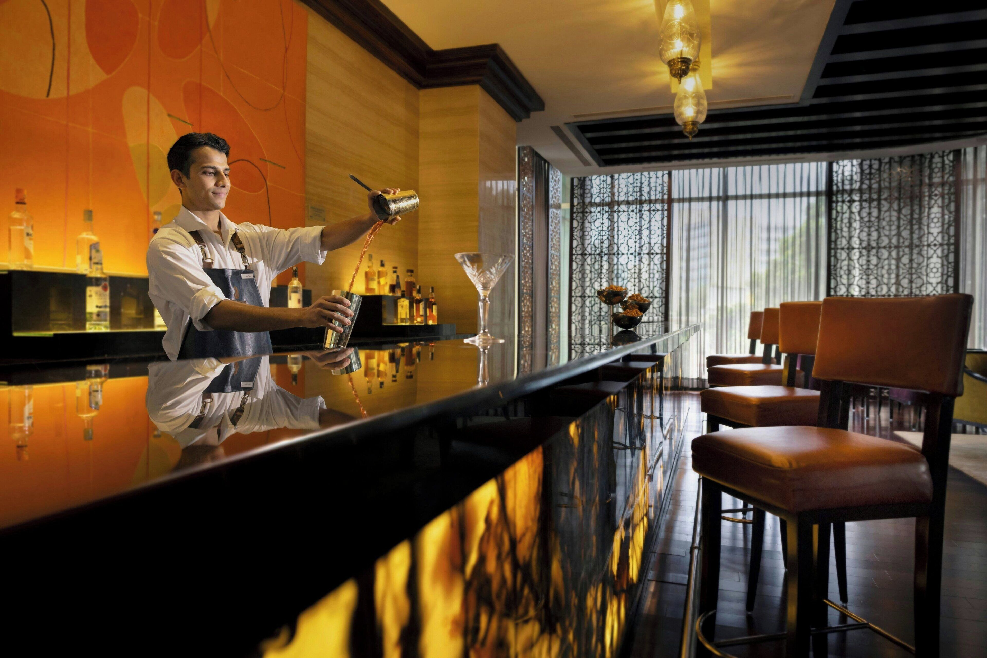 Zona de bar con mostrador negro pulido, un camarero y varios taburetes.