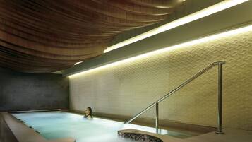 A modern indoor swimming pool with a unique wooden ceiling design and a geometric wall pattern.