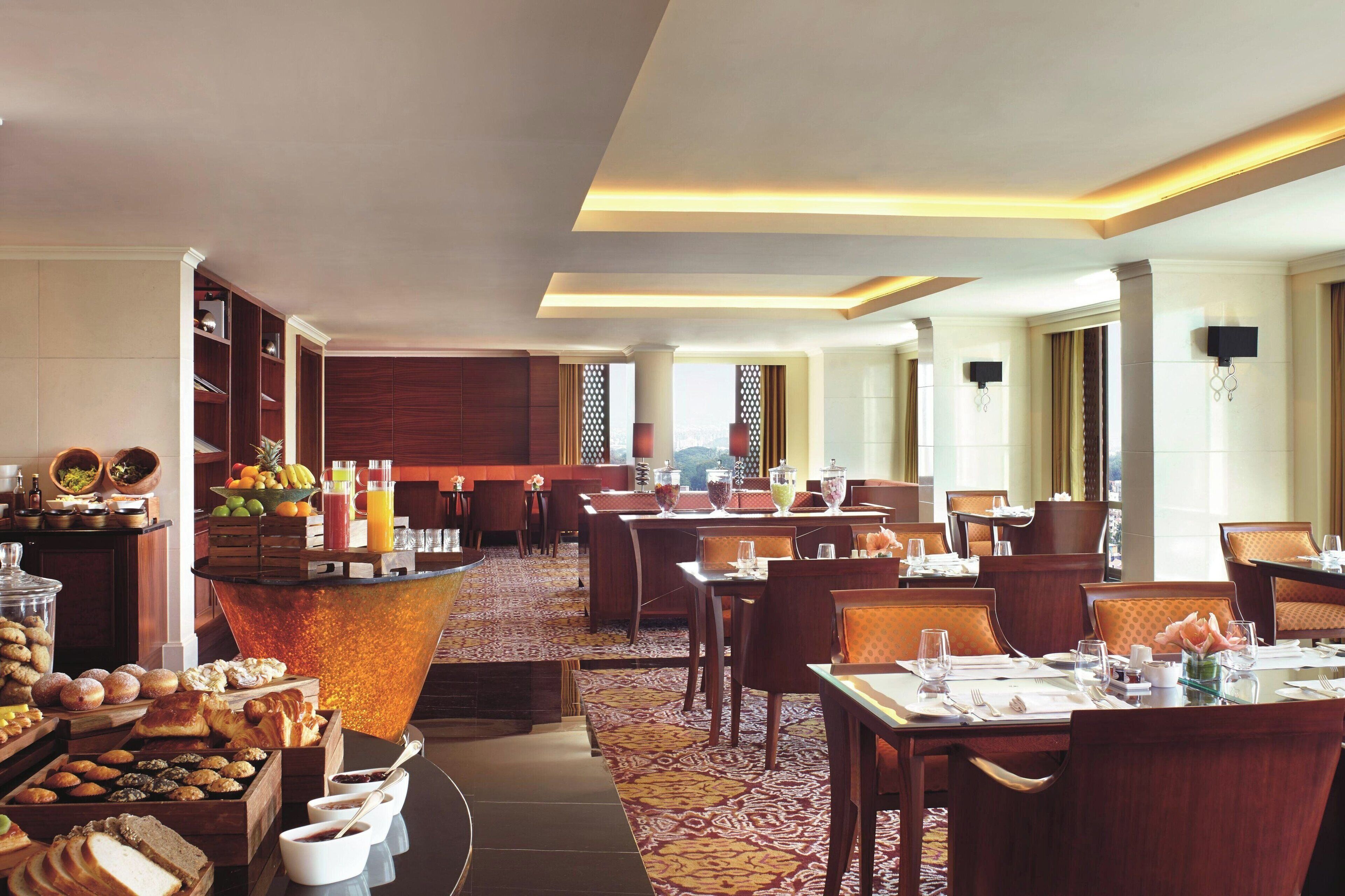 Un comedor de hotel con servicio de buffet, varias mesas y una zona de bar central.