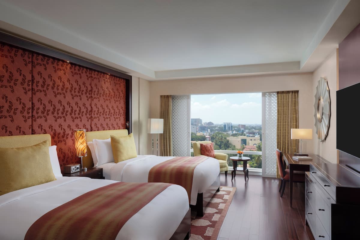 Quarto de hotel com duas camas, uma escrivaninha, uma cadeira, televisão e vista para a cidade.