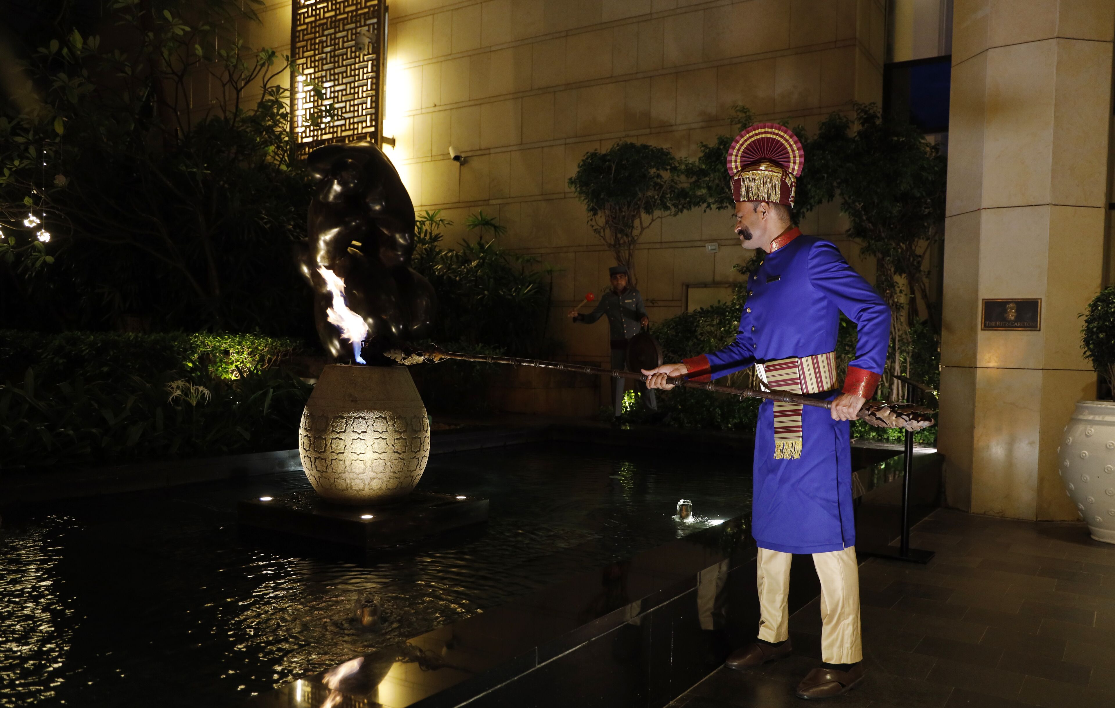 A fountain with a statue, a person in traditional attire, and a building with a plaque.