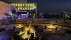 A rooftop lounge with a fire pit, seating, and a view of the cityscape.