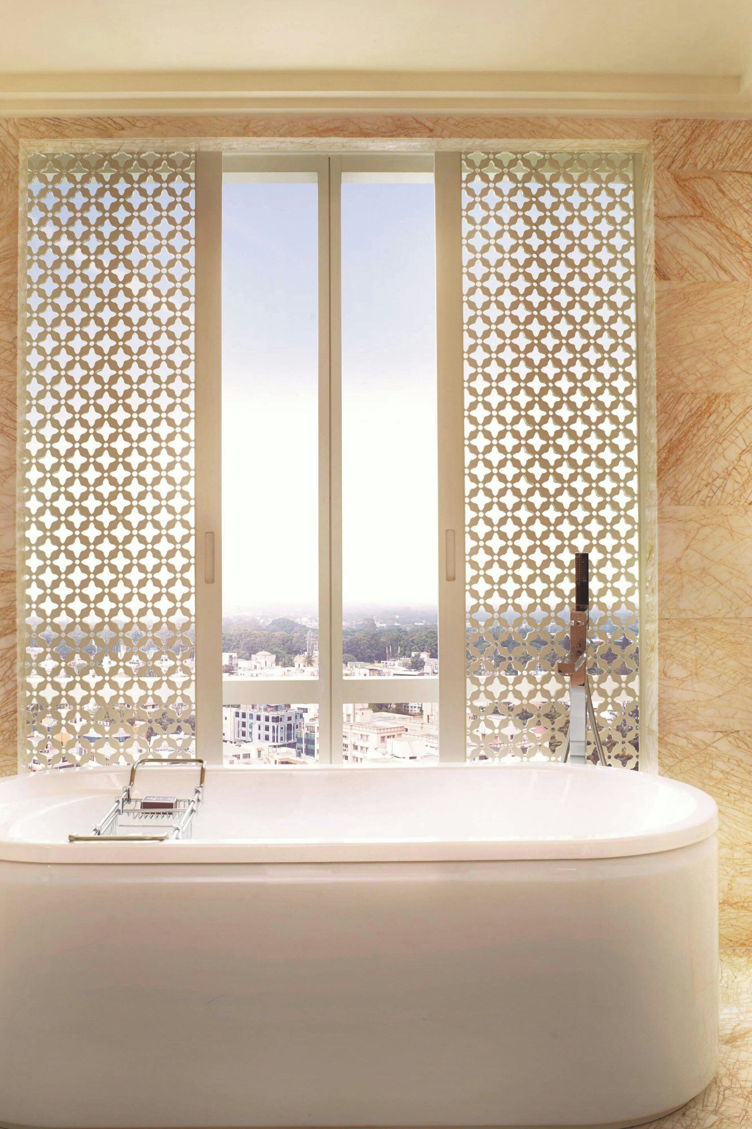 Ein Badezimmer mit einer großen Badewanne, einem Fenster mit dekorativer Abschirmung und Blick auf Gebäude.