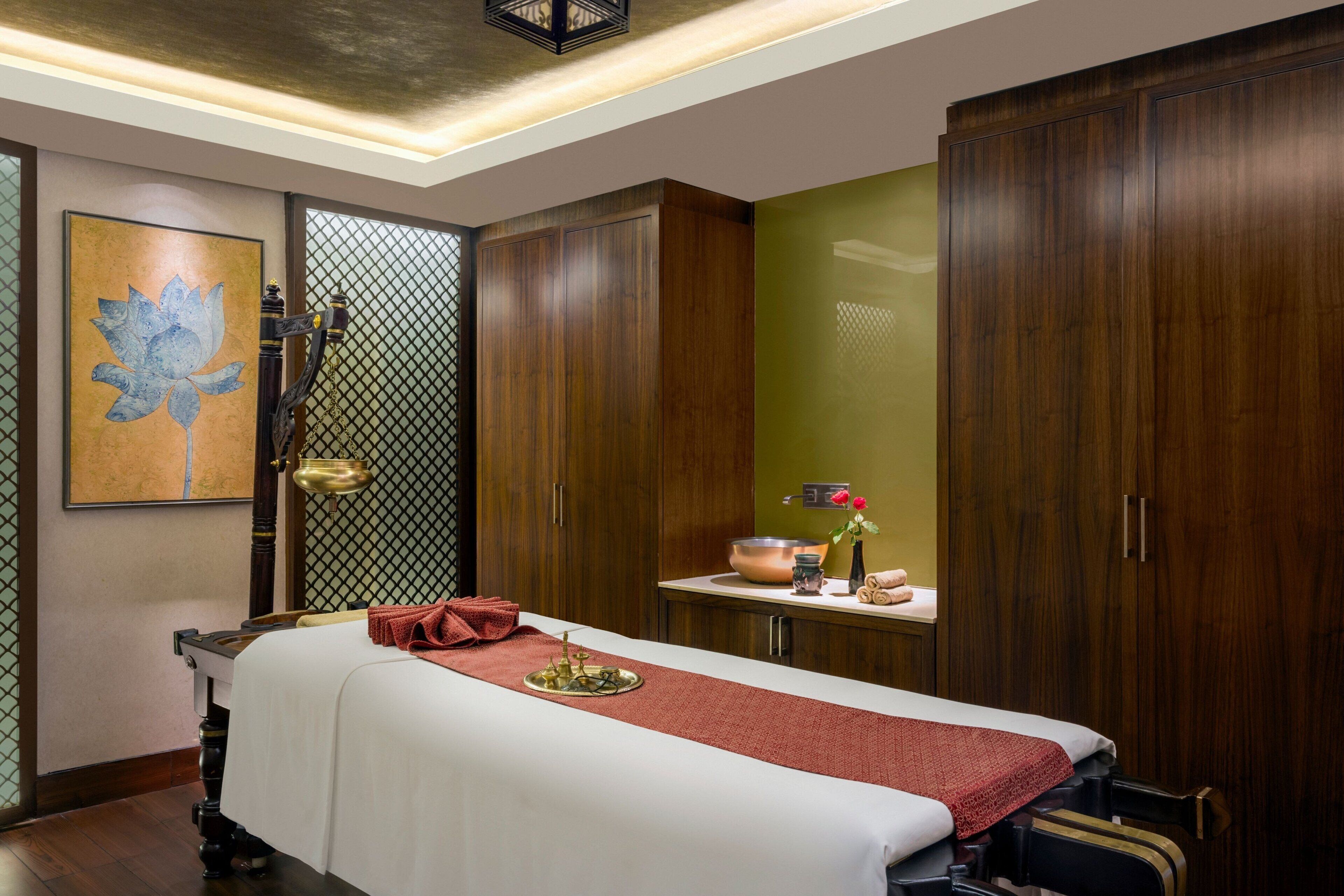 A room with a massage table, wooden cabinets, a green wall, and a framed artwork.