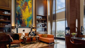 A spacious room with a large window, a colorful abstract painting, a wooden bookshelf, and a seating area with a sofa and chairs.