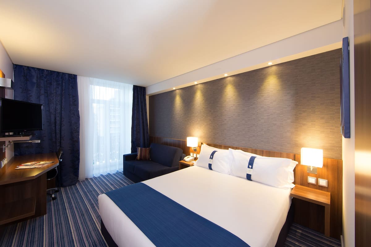 Una habitación de hotel con una cama grande, un escritorio, una silla y un televisor.
