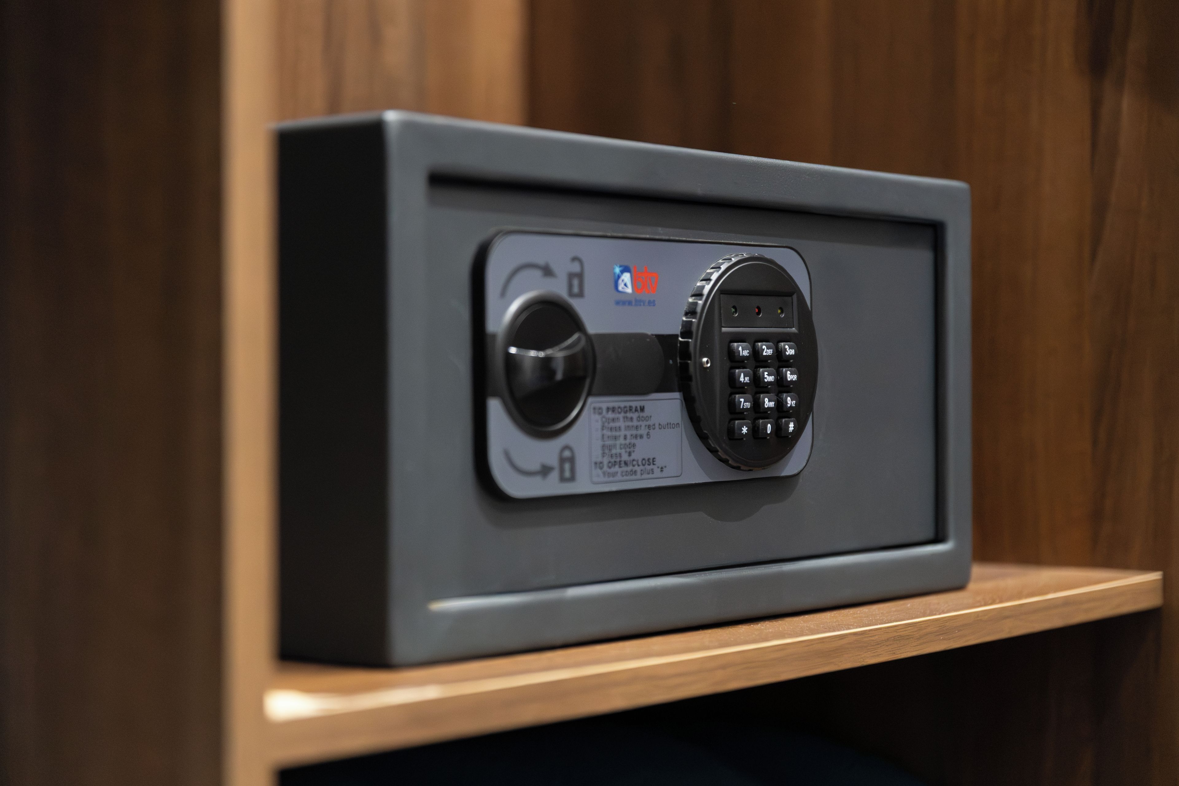 A safe with a combination dial and a keypad, placed on a wooden shelf.