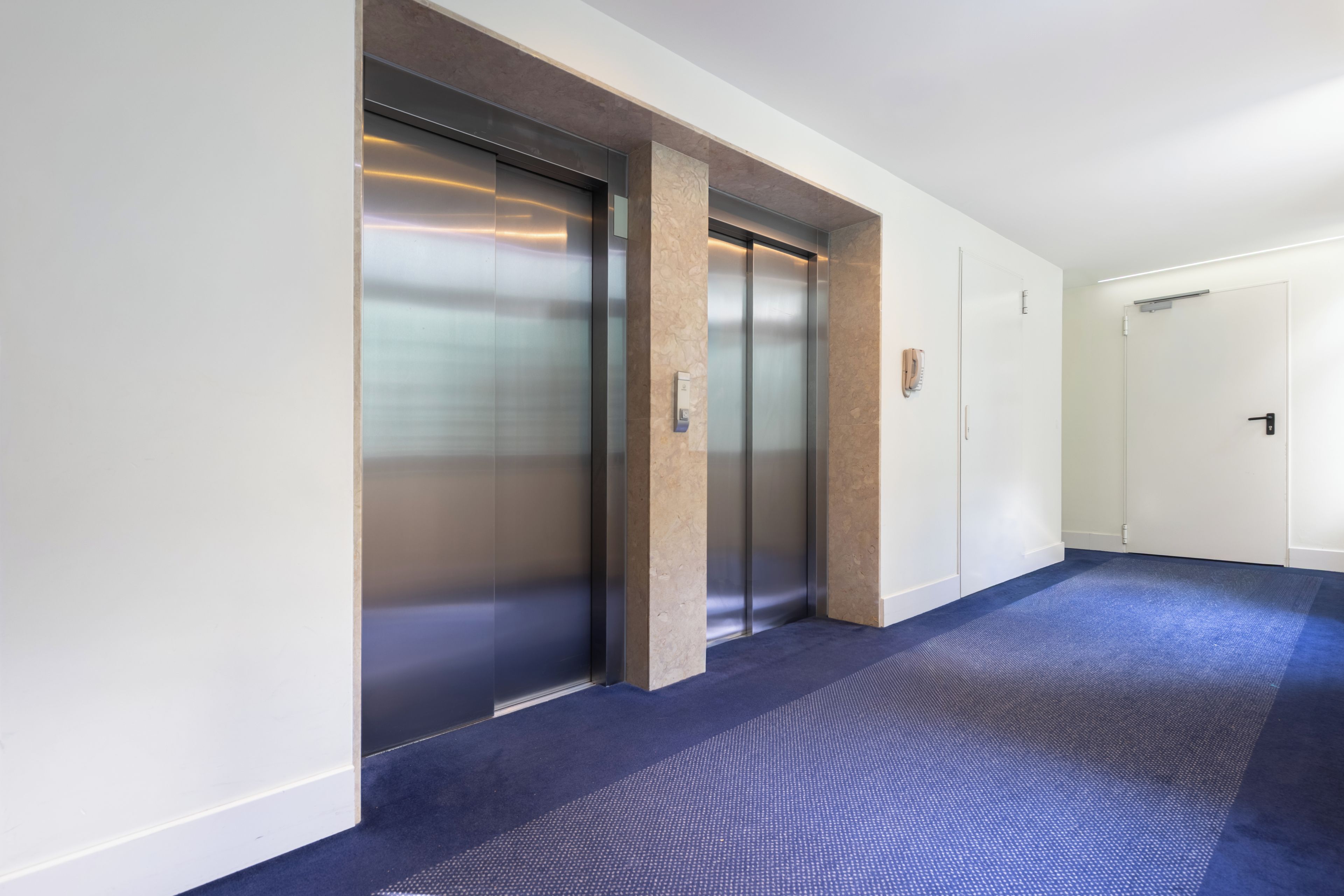 A hallway with two elevators and a door at the end.