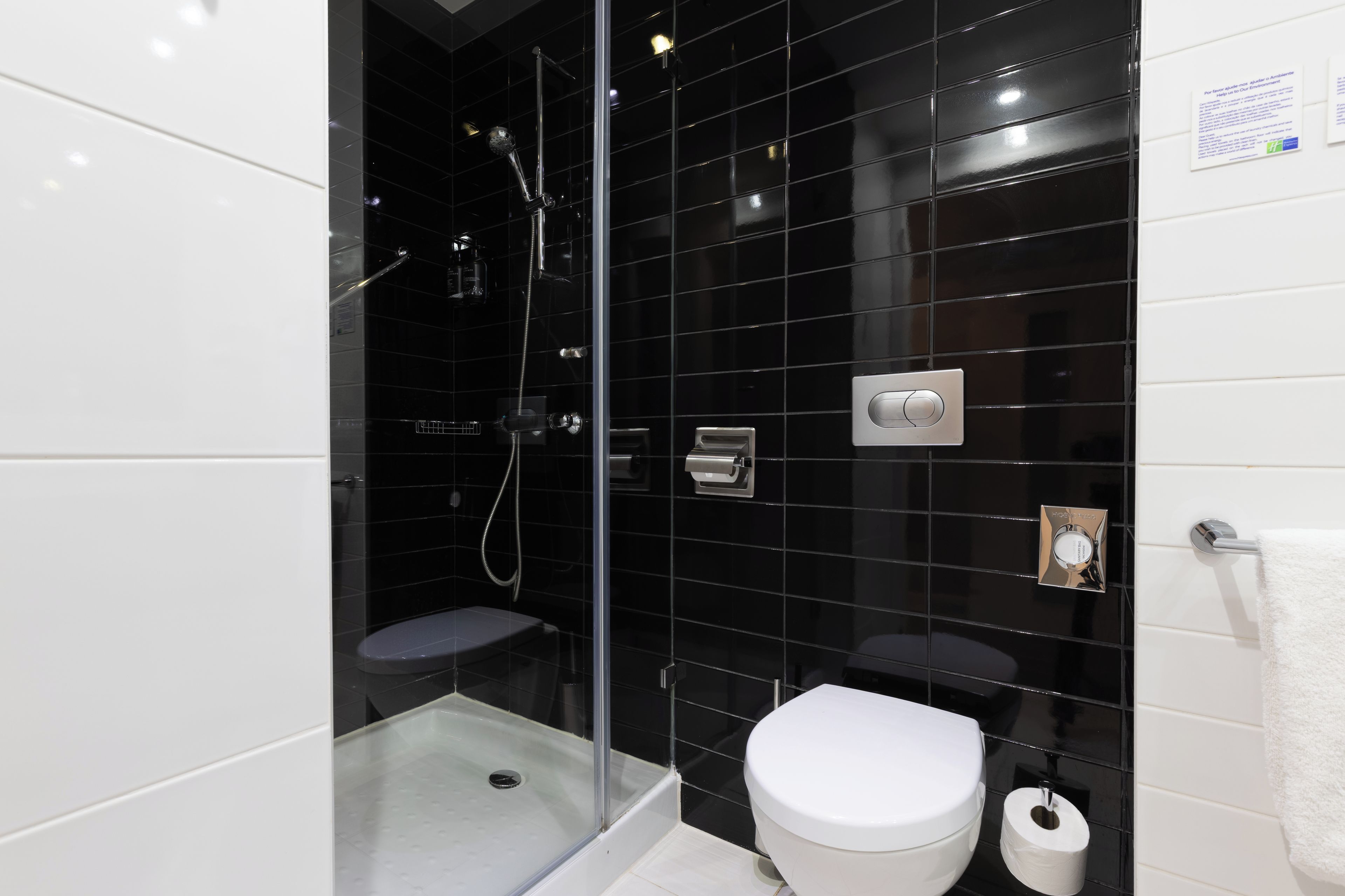 Een moderne badkamer met een douchecabine van glas, een wit toilet en een wand betegeld met zwart tegels.