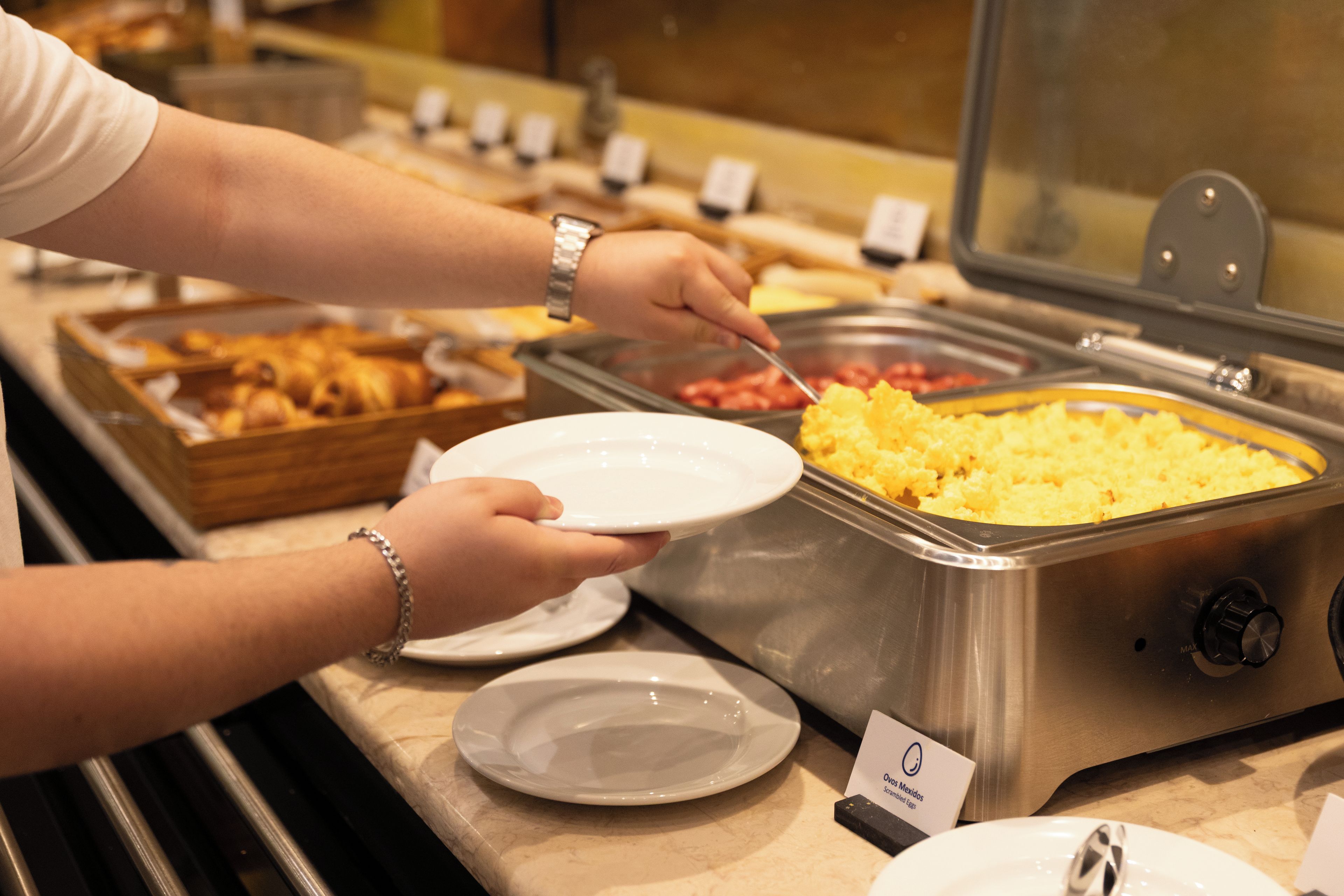 A buffet setup with various food items and a person serving themselves.