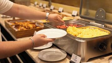 A buffet setup with various food items and a person serving themselves.
