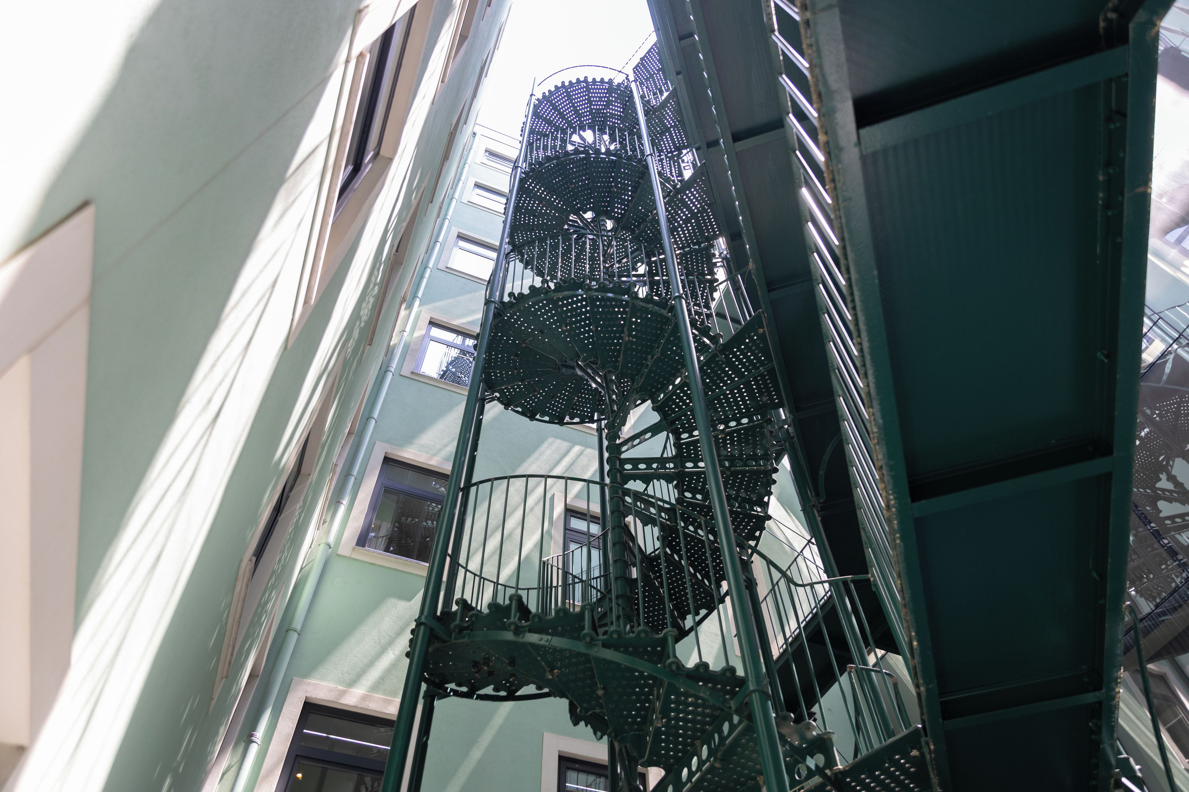 A spiral staircase with a metal railing, surrounded by a building with multiple windows.