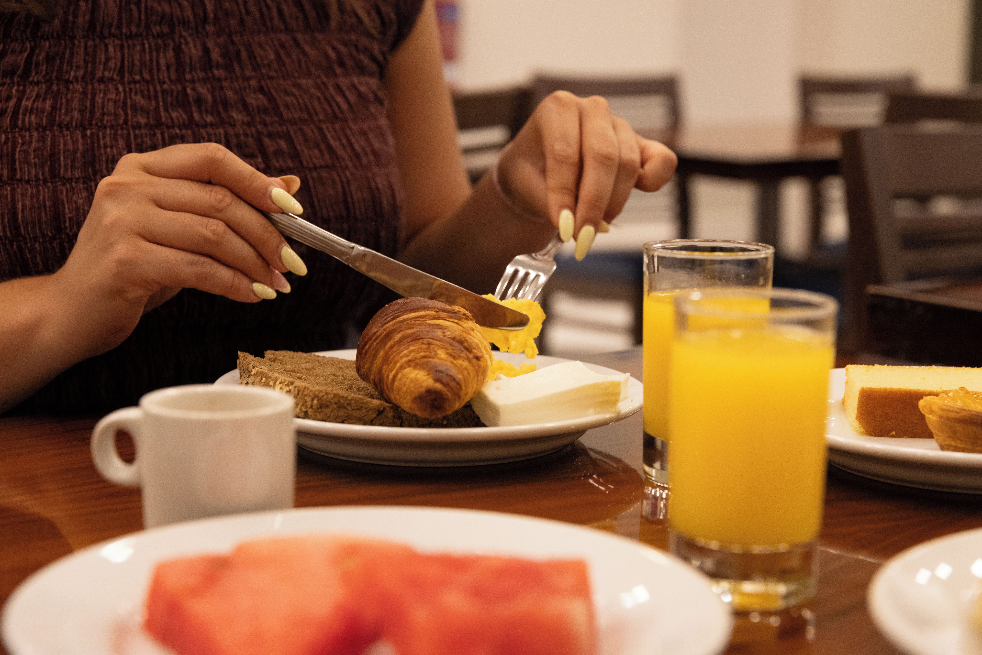 A person cutting a croissant with a knife on a plate with a glass of orange juice.