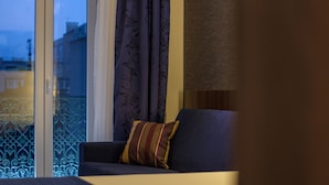 A hotel room with a bed, a sofa, and a view of buildings through a window with a curtain. - Holiday Inn Express Lisbon, Av. Liberdade by IHG (Lisbon)