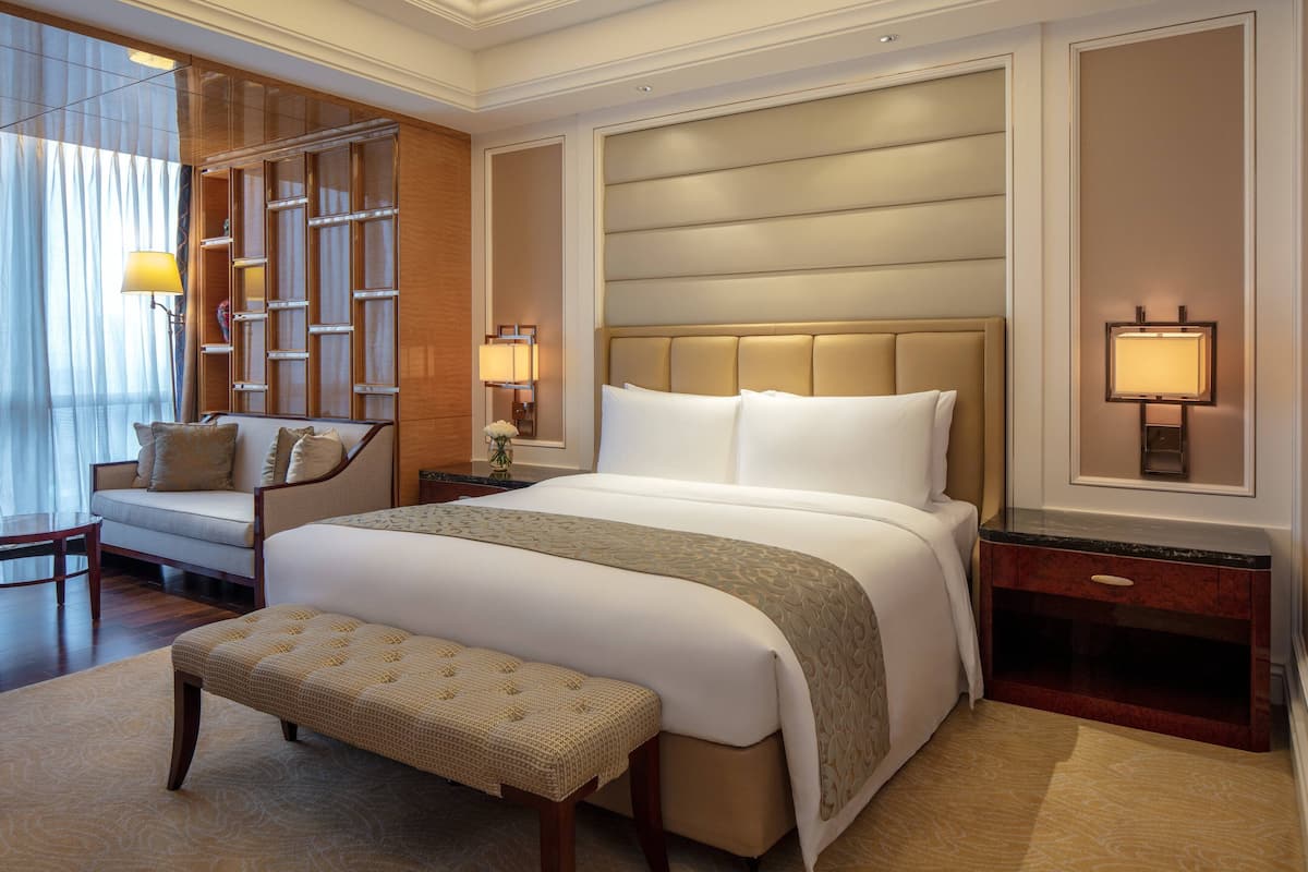 Une chambre d’hôtel avec un grand lit, une banquette, une table de chevet et une lampe fixée au mur.