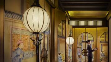 A traditional interior with a person walking, ornate wall decorations, and hanging lamps.