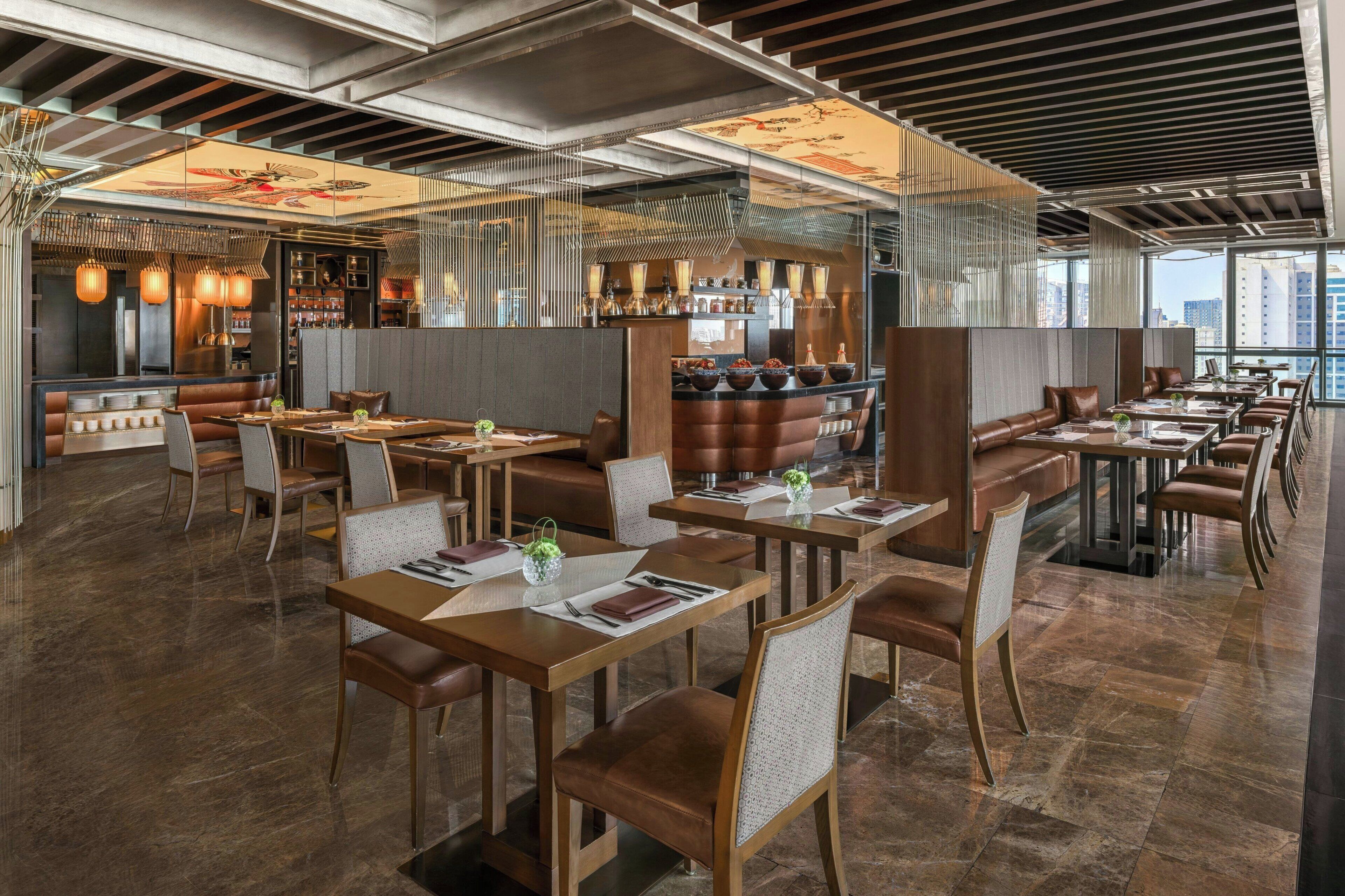 Un restaurant moderne avec un intérieur élégant, caractérisé par de hauts plafonds, des poutres apparentes et une variété d’aménagements, notamment des banquettes et des tables.
