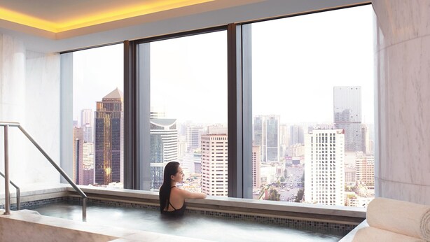 Un área de spa con un ventanal que ofrece vistas a la ciudad, una bañera de mármol y un perchero.