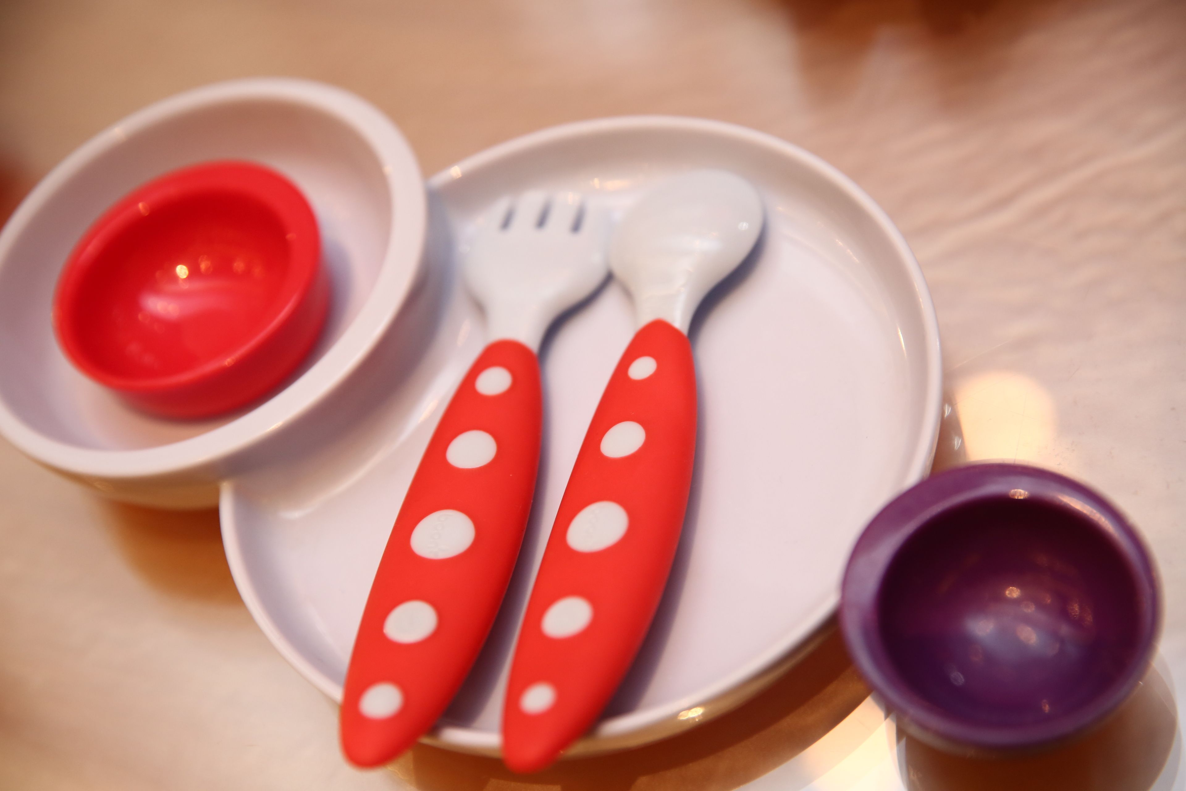 Una vajilla con un plato blanco, cubiertos con lunares rojo y blanco, y un bol rojo y morado.