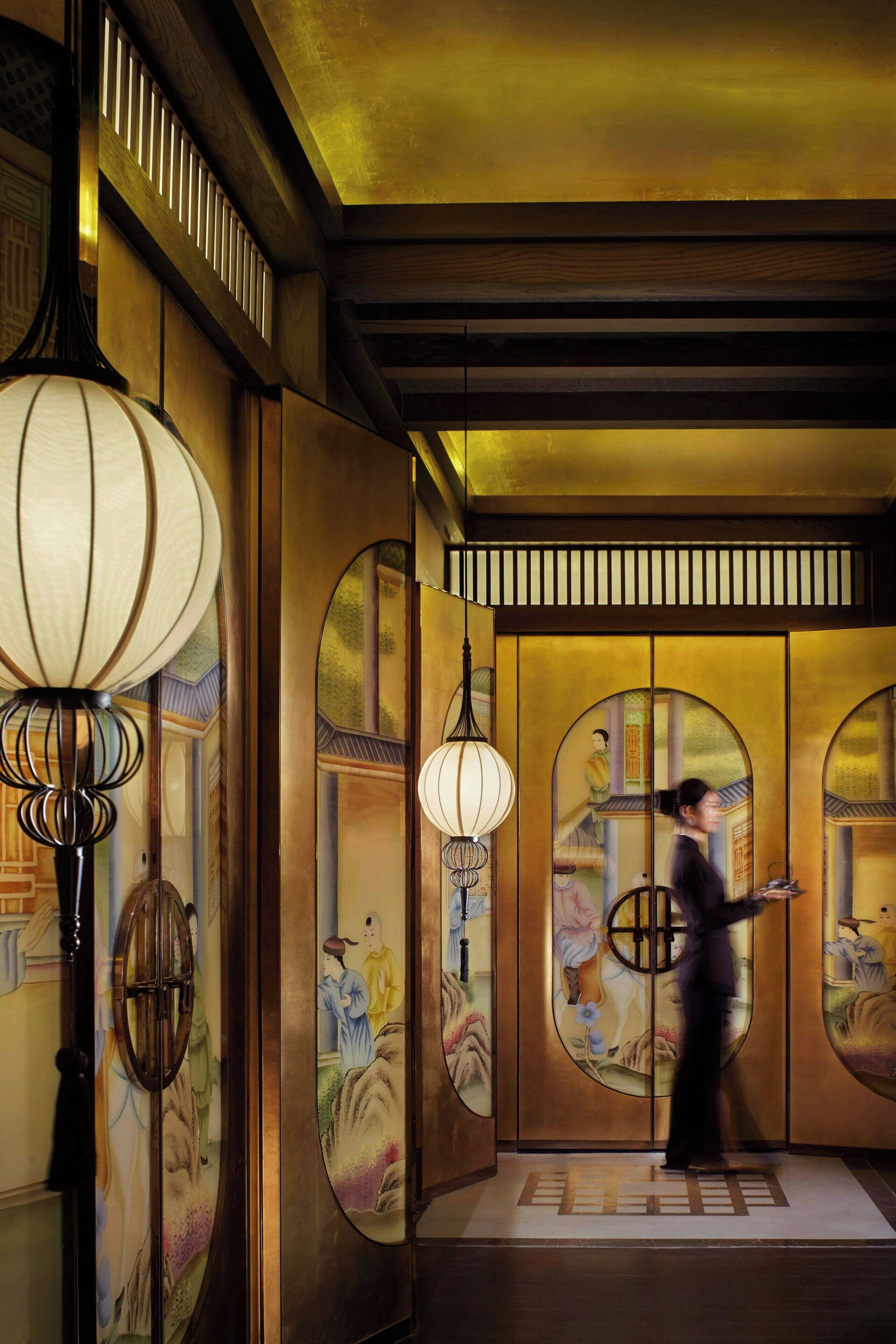 A traditional interior with wooden paneling, a hanging lamp, and a person walking.