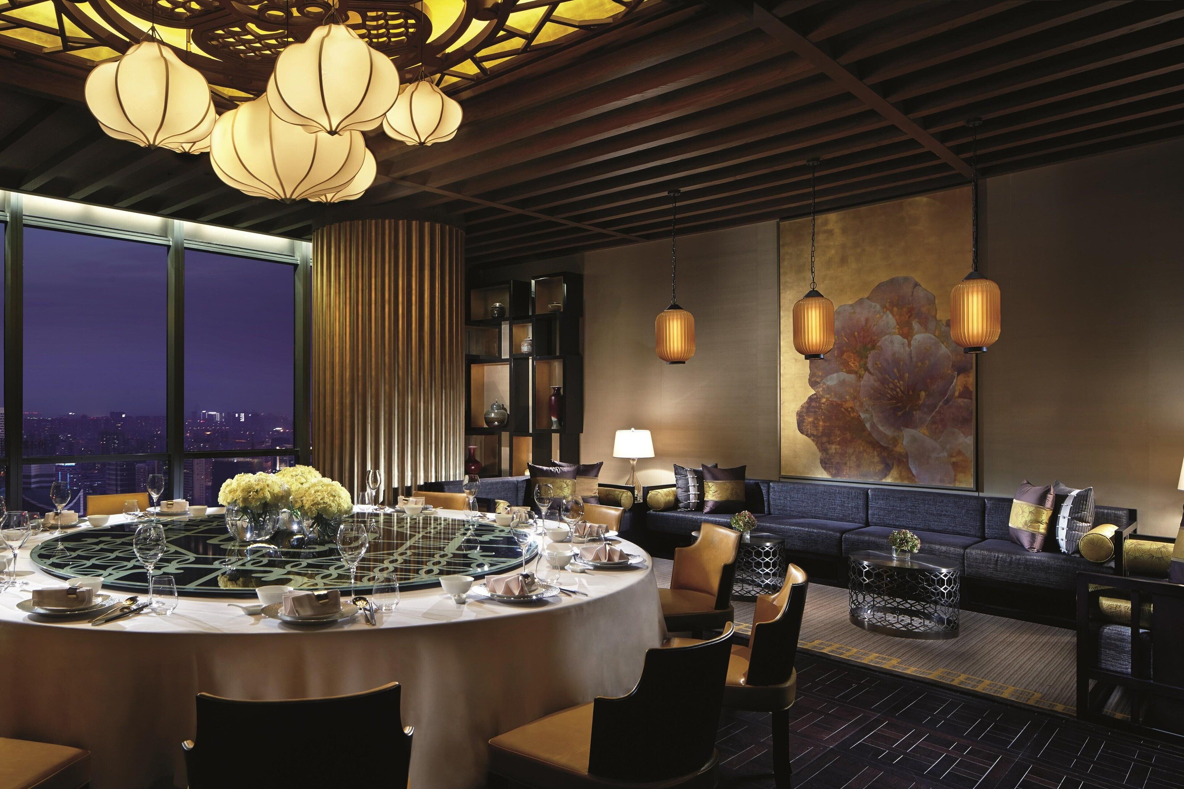 A dining area with a round table set for a meal, a sofa, and a large window with a city view.