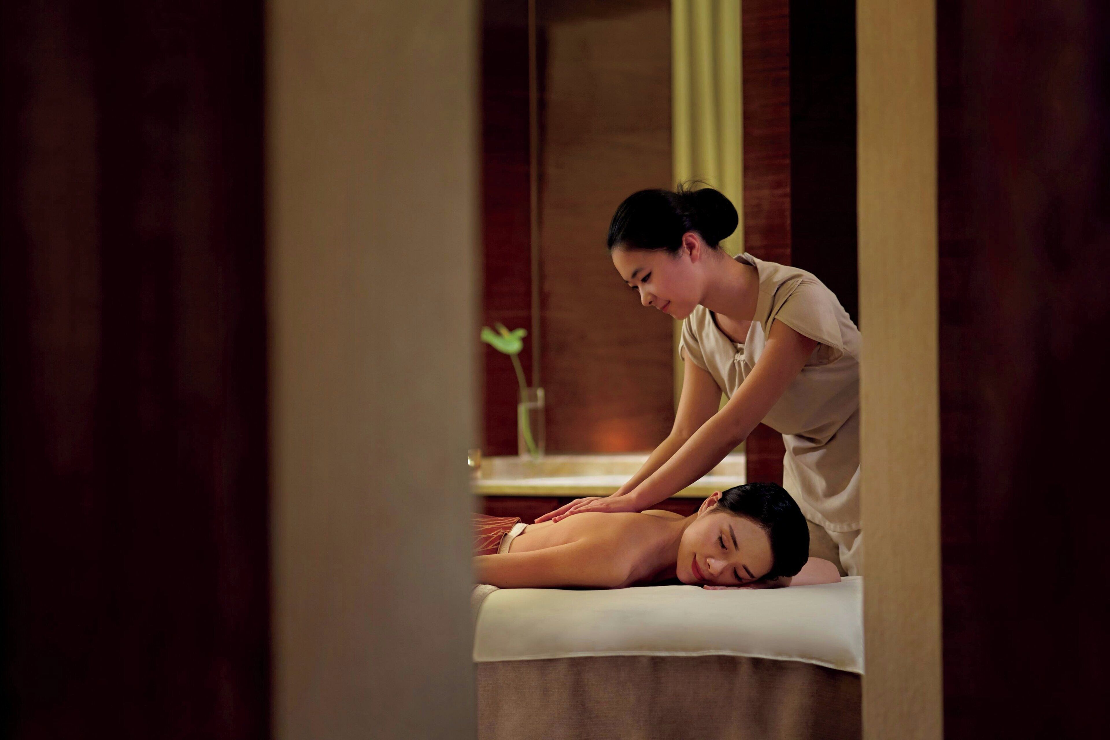 A massage therapy session in a room with a wooden floor and a large mirror on the wall.