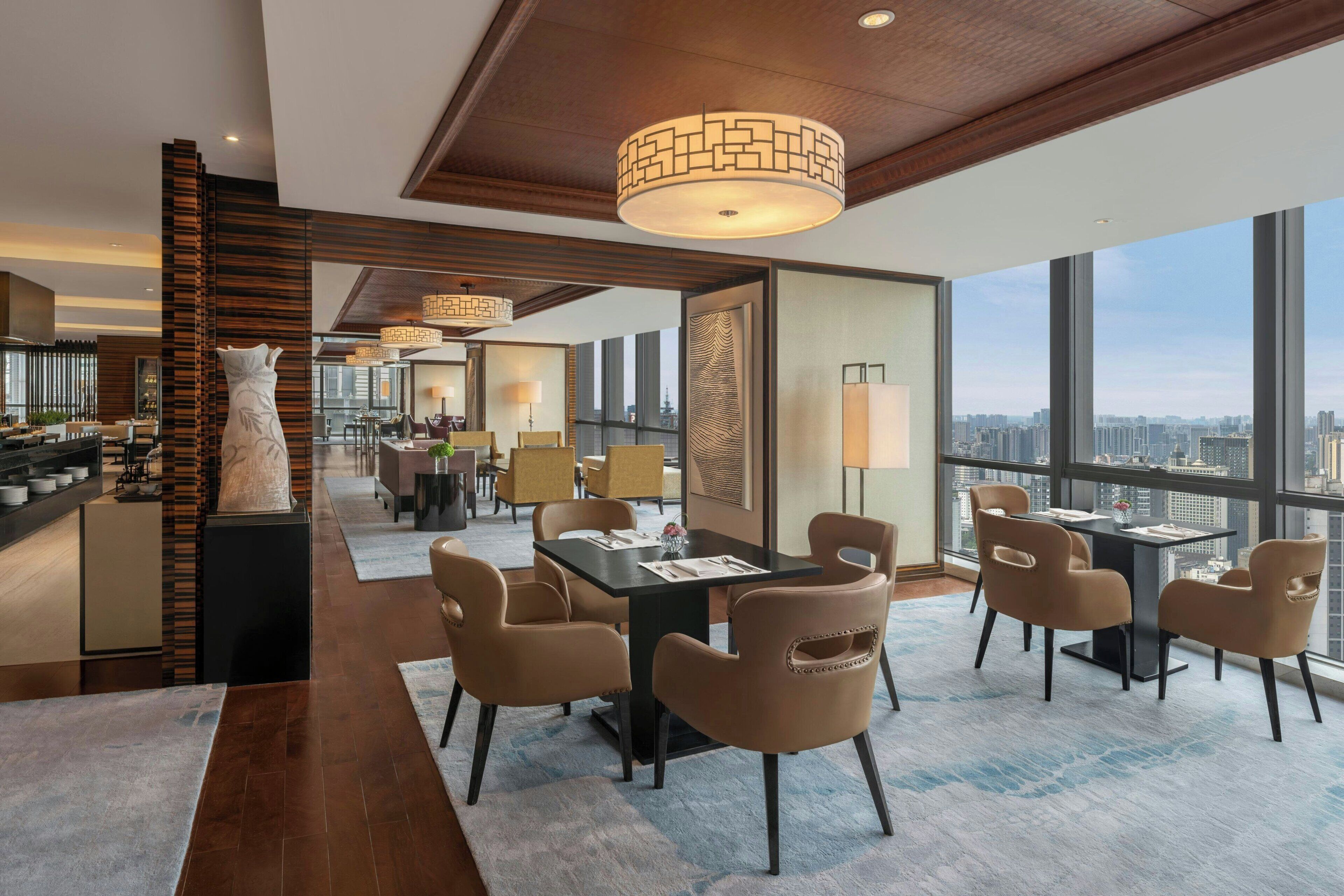 A modern hotel interior with a dining area, kitchen, and large windows offering city views.