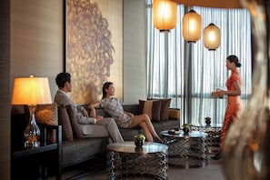 A modern hotel lobby with a sofa set, round tables, and decorative lamps.