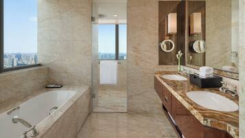 A modern bathroom with a bathtub, two sinks, a large mirror, and a view of the city through a glass door.