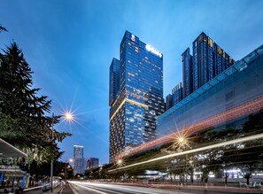 A cityscape with modern high-rise buildings, a well-lit street, and a pedestrian walkway.