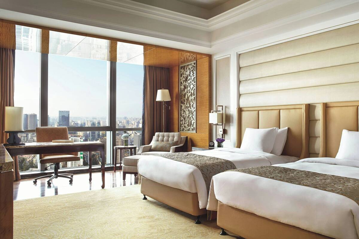 Une chambre d’hôtel avec deux lits, un bureau, une chaise et une vue sur la ville.