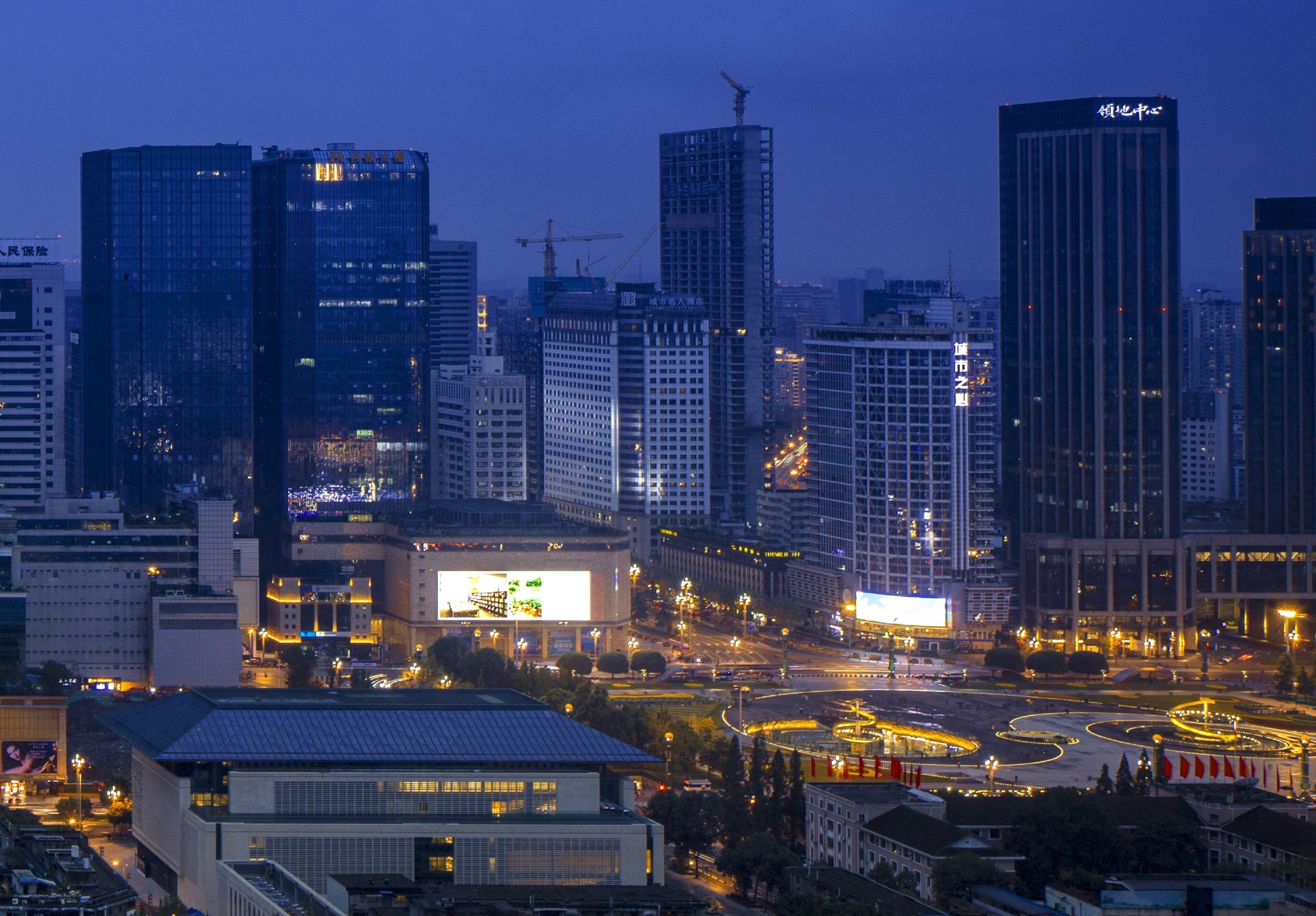 A cityscape at dusk with illuminated buildings and a busy intersection.