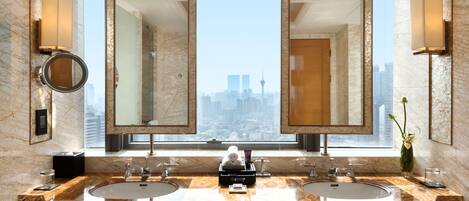 Ein modernes Badezimmer mit zwei Waschbecken, großen Spiegeln und Blick auf eine Stadtkulisse durch ein großes Fenster.