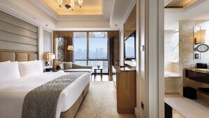 Habitación de hotel con una cama grande, un escritorio, una silla, una mesita, un espejo y vistas a la ciudad.