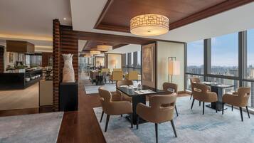 Un moderno vestíbulo de hotel con comedor, ventanas amplias y vista a la ciudad.