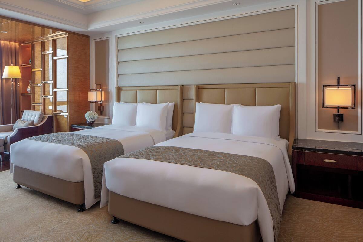 Une chambre d’hôtel avec deux lits, un bureau, une chaise et une lampe.