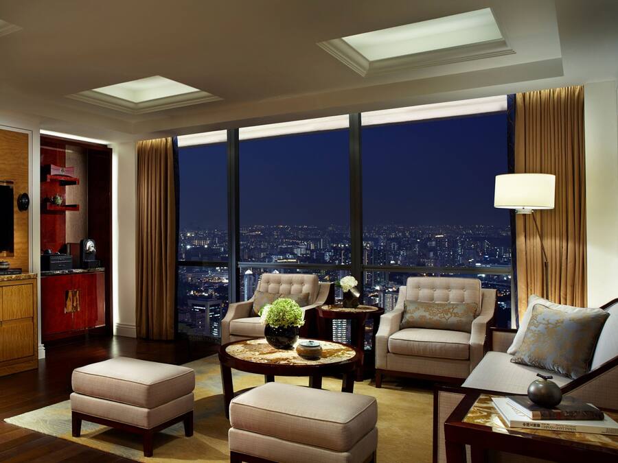 A spacious living room with a city view, a television, and a red minibar.