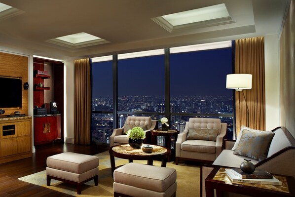Amplia sala de estar con vista a la ciudad, televisor y un minibar rojo.