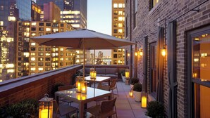 A rooftop terrace with a table and chairs, surrounded by lanterns and potted plants, overlooking a cityscape at dusk. - WestHouse Hotel New York, an SLH Hotel (New York)